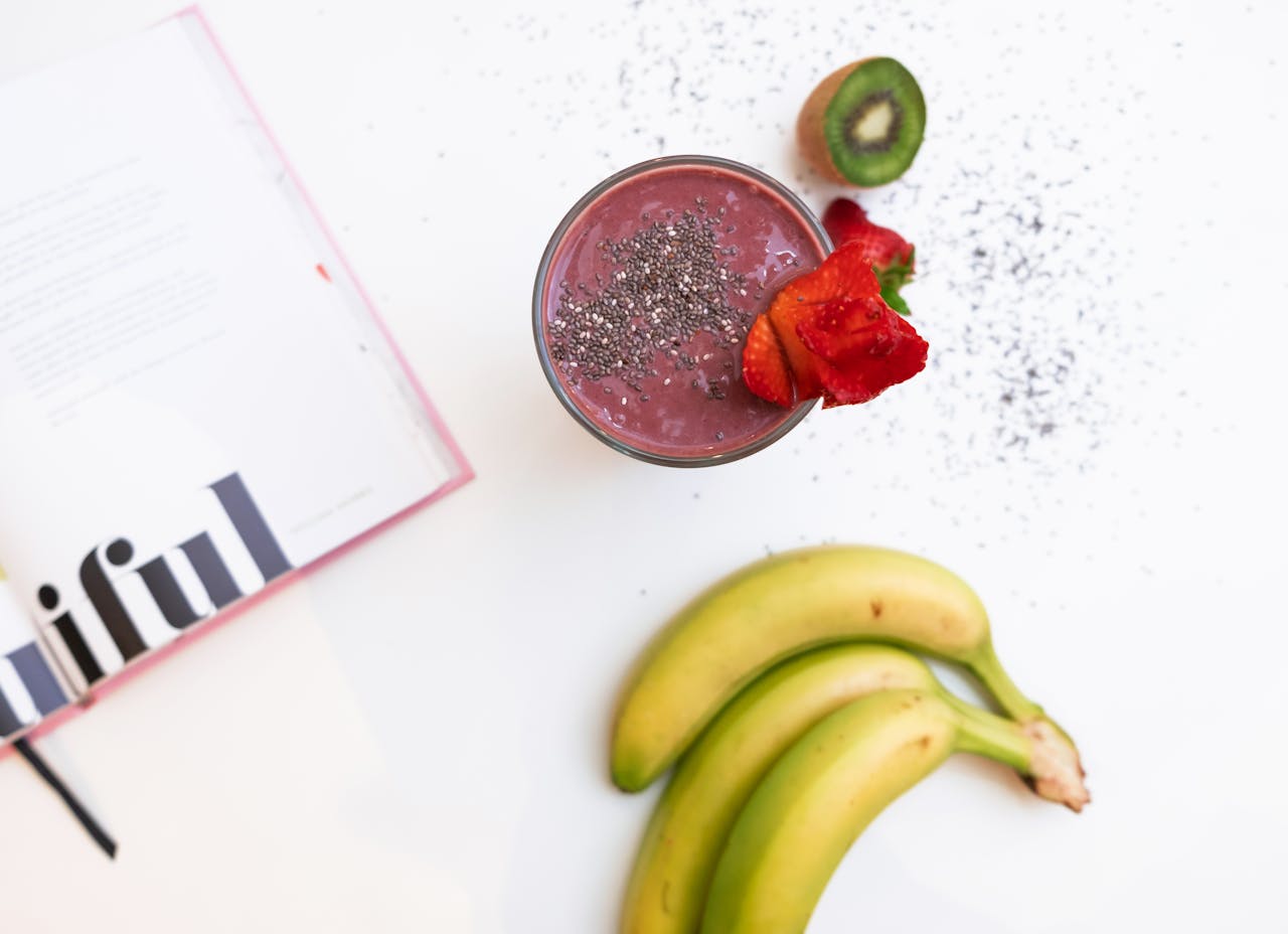 A delicious banana and berry smoothie topped with chia seeds, accompanied by fresh fruits and a magazine.