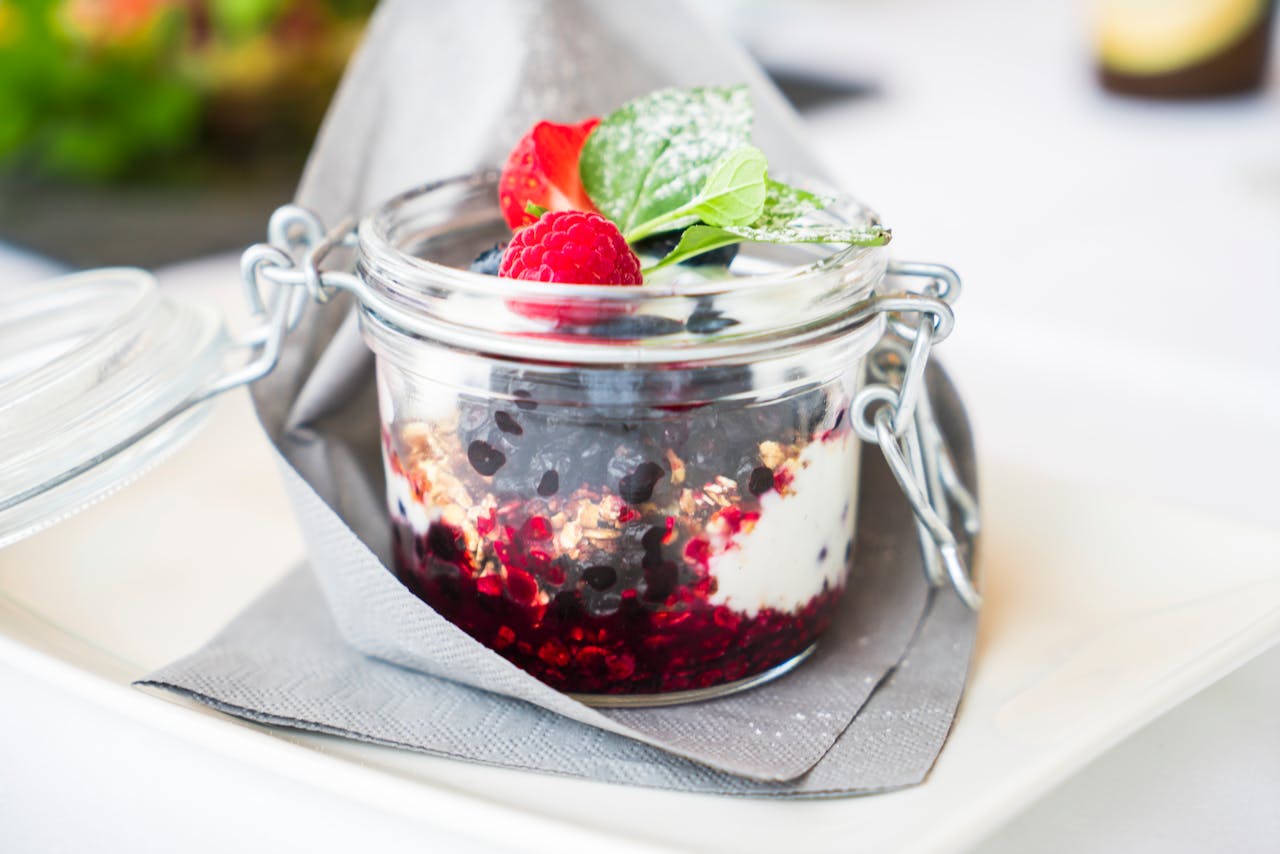 Homemade berry dessert with cream and mint in a glass jar, perfect for breakfast.